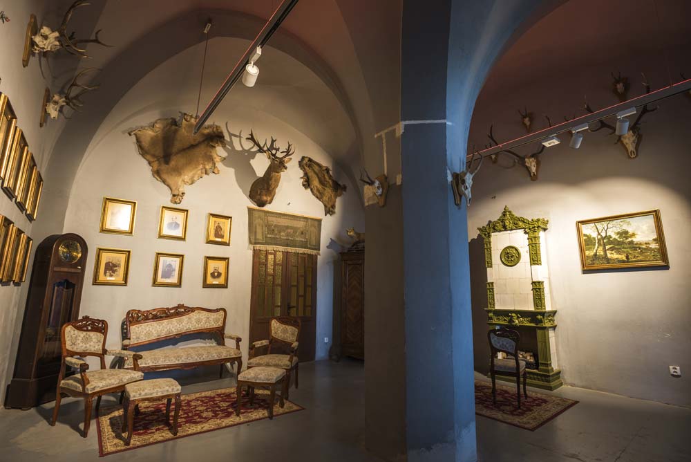 Zabytkowa komnata w Pałacu Marianny Orańskiej, Kamieniec Ząbkowicki – wnętrze z myśliwskimi trofeami, stylowymi meblami i zielonym piecem kaflowym.