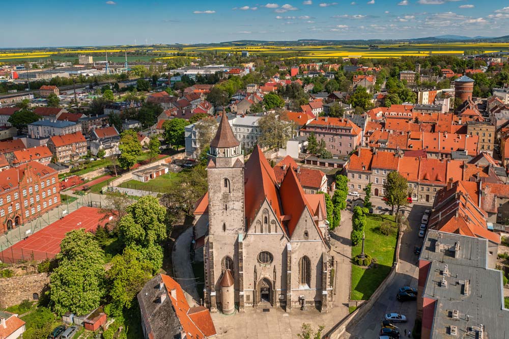 Z lotu ptaka widać kościół św. Marcina w Jaworze, którego wieża dominuje nad historycznym centrum miasta. Wokół rozciągają się ulice i kamienice z ceglanymi dachami.