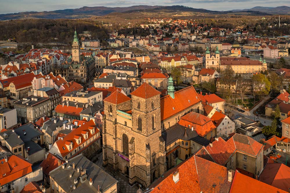 Kościół Najświętszej Maryi Panny w Kłodzku widziany z lotu ptaka, z górującą kamienną wieżą i panoramą miasta oraz gór w tle.