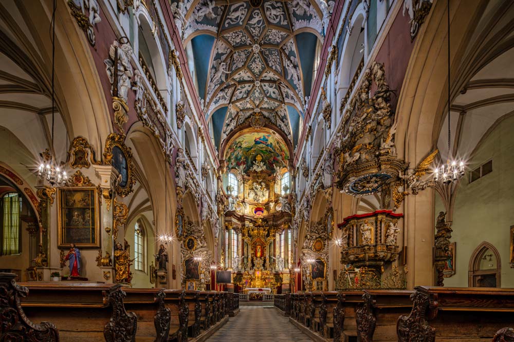 Wnętrze Kościoła Najświętszej Maryi Panny w Kłodzku z bogato zdobionym barokowym ołtarzem, złoconymi rzeźbami i malowanym sklepieniem krzyżowym.