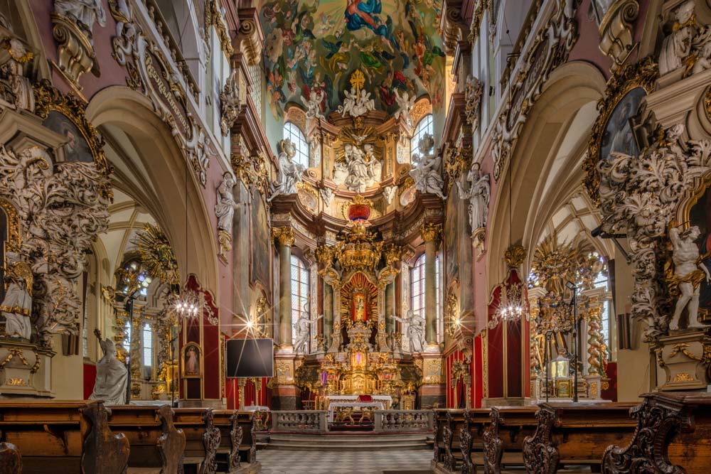 Barokowe wnętrze Kościoła Wniebowzięcia Najświętszej Maryi Panny w Kłodzku z bogato zdobionym ołtarzem, rzeźbami aniołów i malowidłami na sklepieniu.