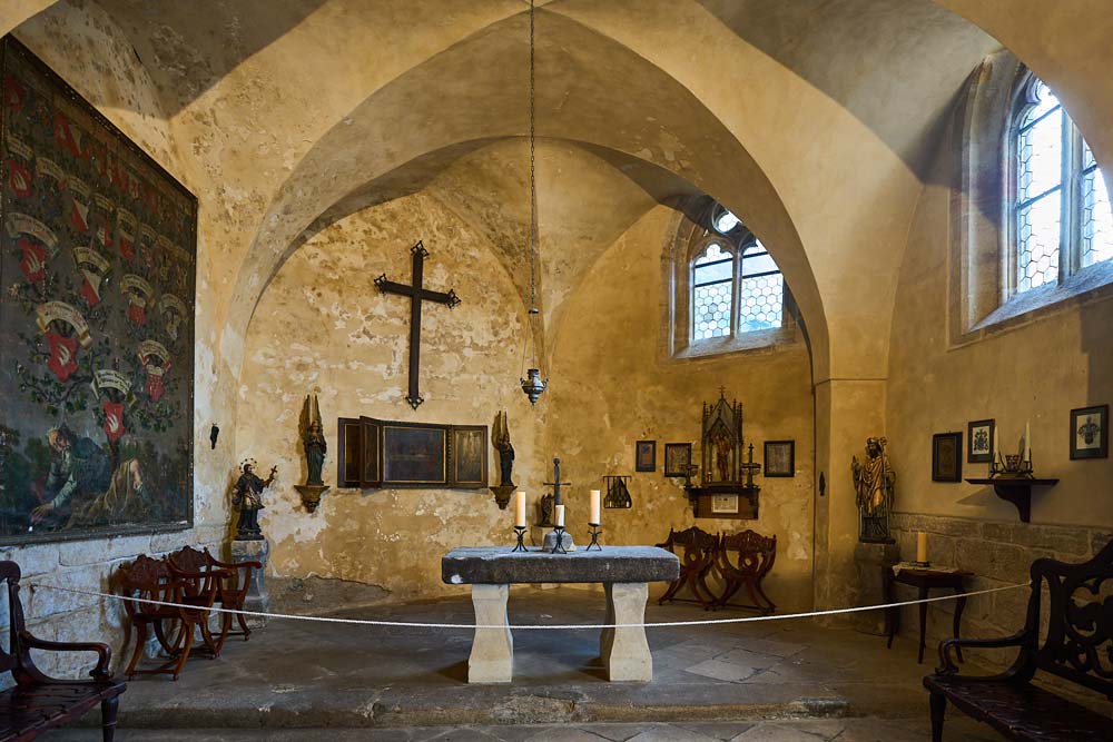 Kaplica zamkowa w Zamku Kost z kamiennym ołtarzem, krzyżem na ścianie i gotyckimi oknami przepuszczającymi ciepłe światło.