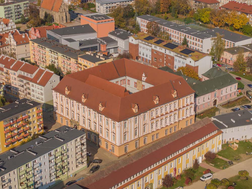 Z lotu ptaka widać dawny barokowy Pałac Biskupi w Nysie, w którym mieści się muzeum. Budynek ma czerwoną dachówkę, ozdobną fasadę i otoczony jest współczesną zabudową mieszkalną.