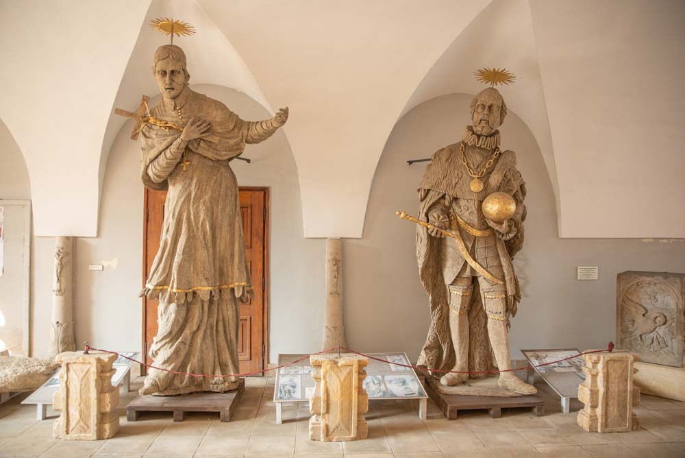 Ekspozycja w dawnym Pałacu Biskupim w Nysie z dwiema dużymi rzeźbami przedstawiającymi postacie w szatach z atrybutami w dłoniach. Rzeźby stoją pod sklepieniem łukowym, otoczone niskimi barierkami.