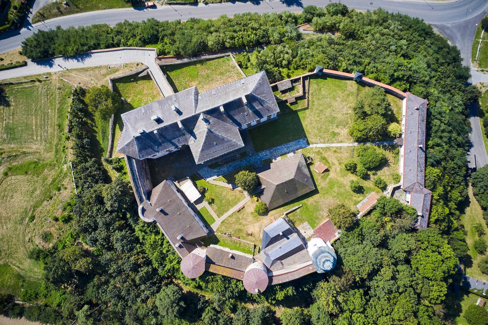 Ujęcie z drona na Pałac Úsov ukazujące kształt kompleksu z murami, wieżami i zielonym dziedzińcem wewnętrznym otoczonym przez zabudowania.