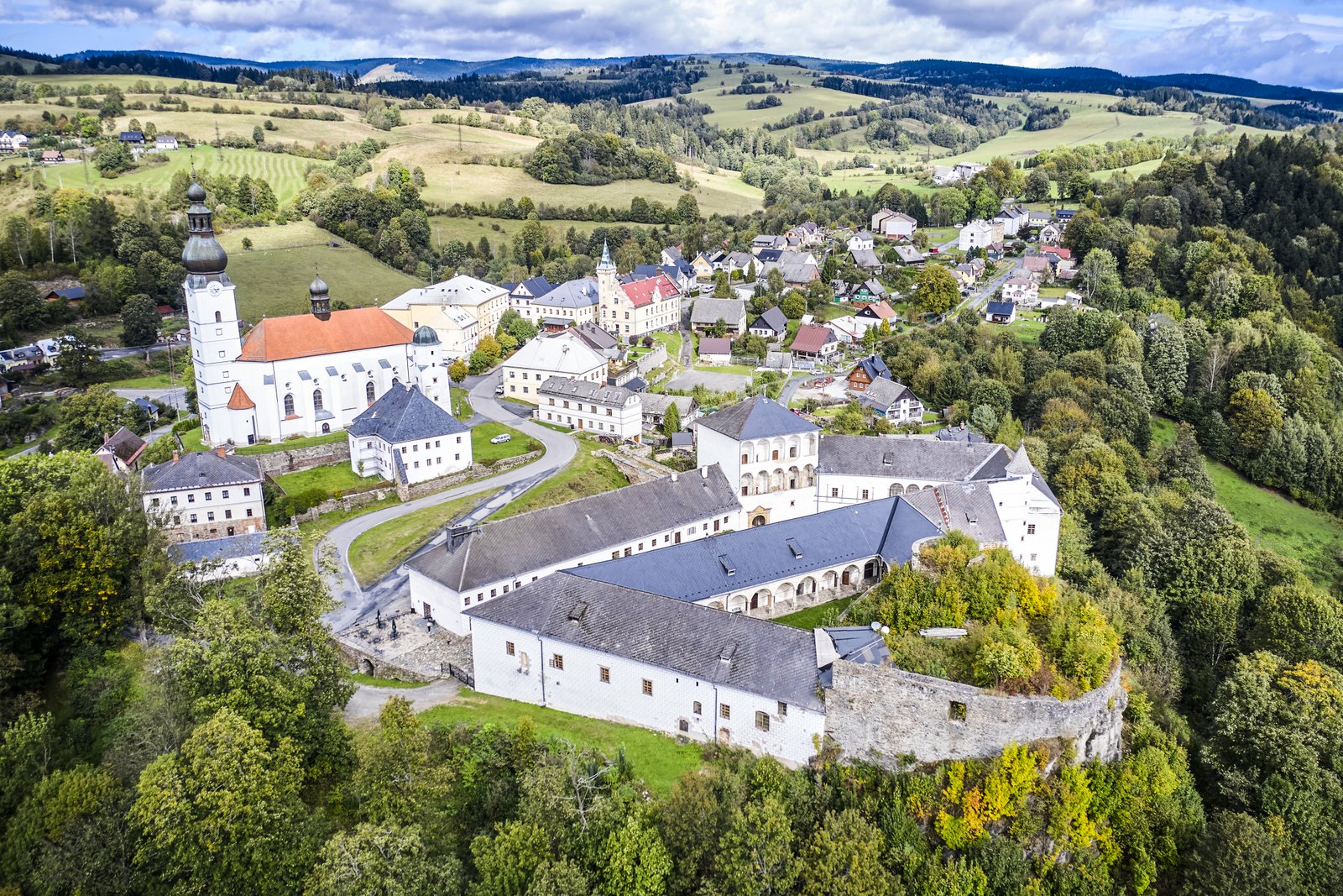 Widok z lotu ptaka na Pałac Kolštejn i wieś Branná – kompleks zamkowy na skale, obok kościół i zabudowania w otoczeniu Jesioników.