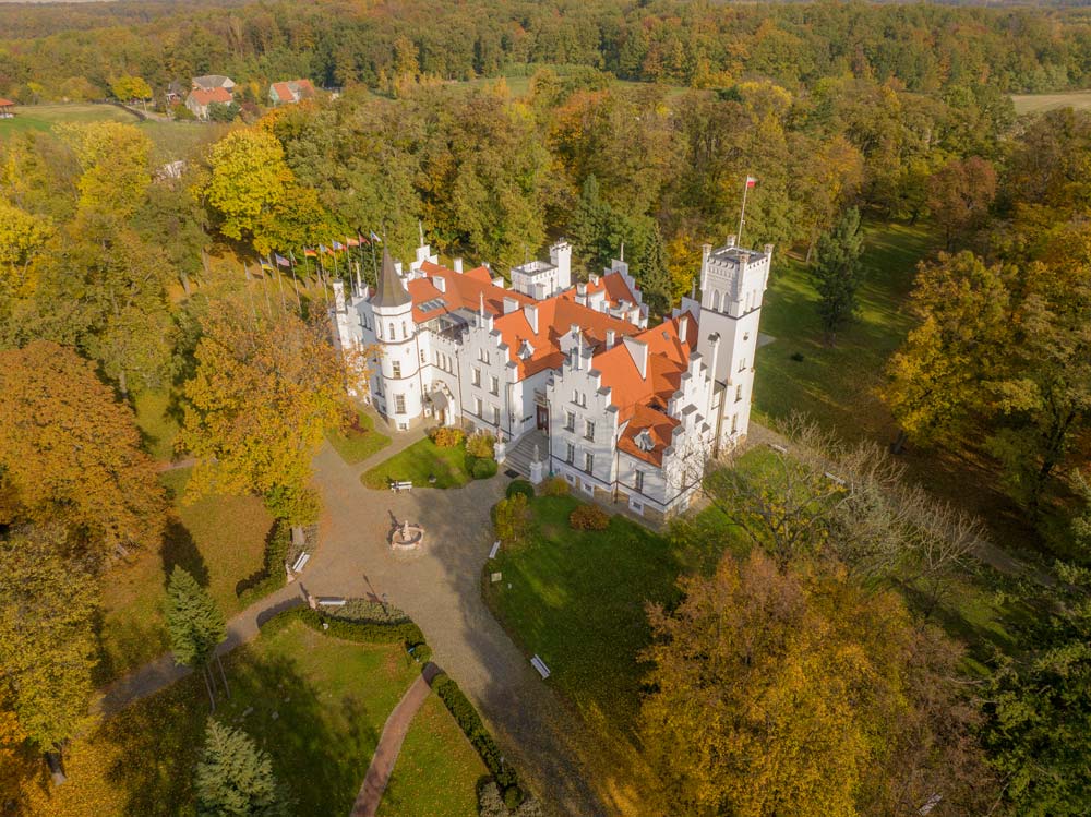 Szeroka panorama lotnicza Pałacu Sulisław otoczonego rozległym, kolorowym jesiennym lasem, ukazująca położenie rezydencji wśród zielonych równin Opolszczyzny.