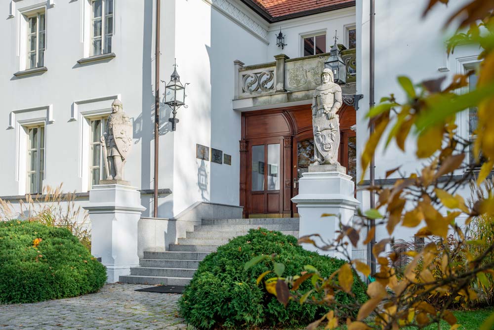 Główne wejście do Pałacu Sulisław z szerokimi schodami, drewnianymi drzwiami i dwiema rzeźbionymi postaciami rycerzy na postumentach