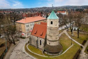 Widok z lotu ptaka na rotundę św. Gotarda i dobudowany kościół w centrum Strzelina, w otoczeniu bloków mieszkalnych, ulic i rozległej panoramy miasta.