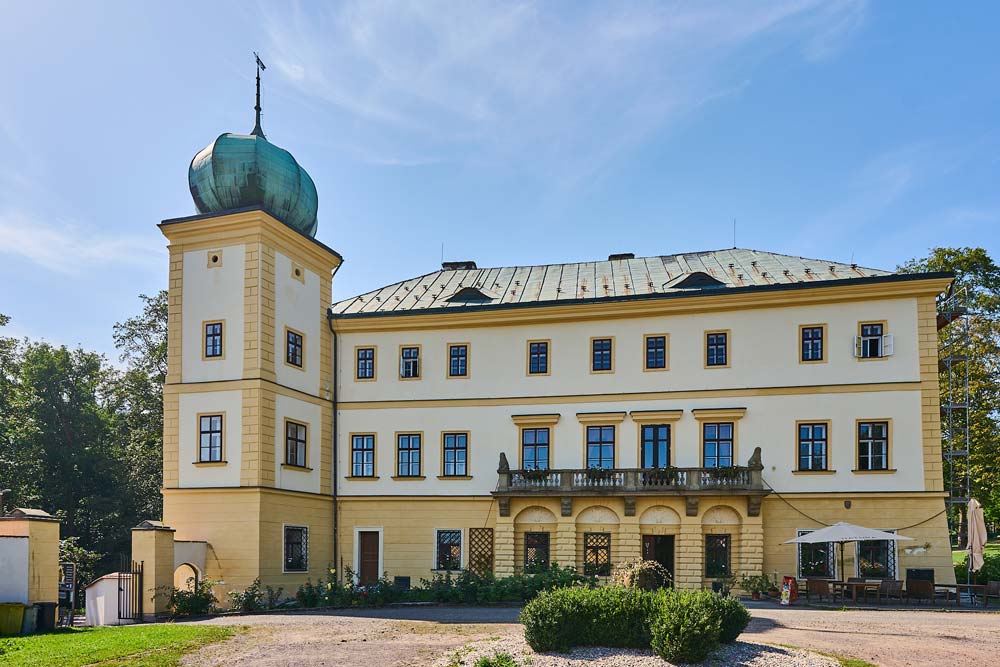 Elewacja zamku Adršpach od strony dziedzińca – jasny budynek z balkonem i arkadami oraz wieża z zielonym hełmem.