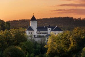 Zamek Rychmburk o zachodzie słońca – sylwetka warowni na tle złotego nieba i ciemnego pasma lasu.