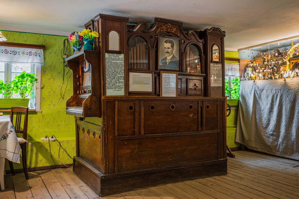 Zabytkowe, drewniane organy w chacie ruchomej szopki w Czermnej; na froncie portret twórcy i tablice z opisami, obok okno i fragment ekspozycji.