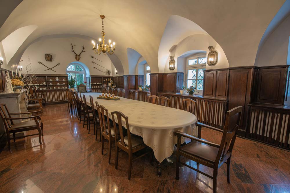 Jasna sala w zamku w Rogowie Opolskim z ustawionymi stołami w podkowę, krzesłami w pasy i żyrandolami pod okrągłym plafonem.