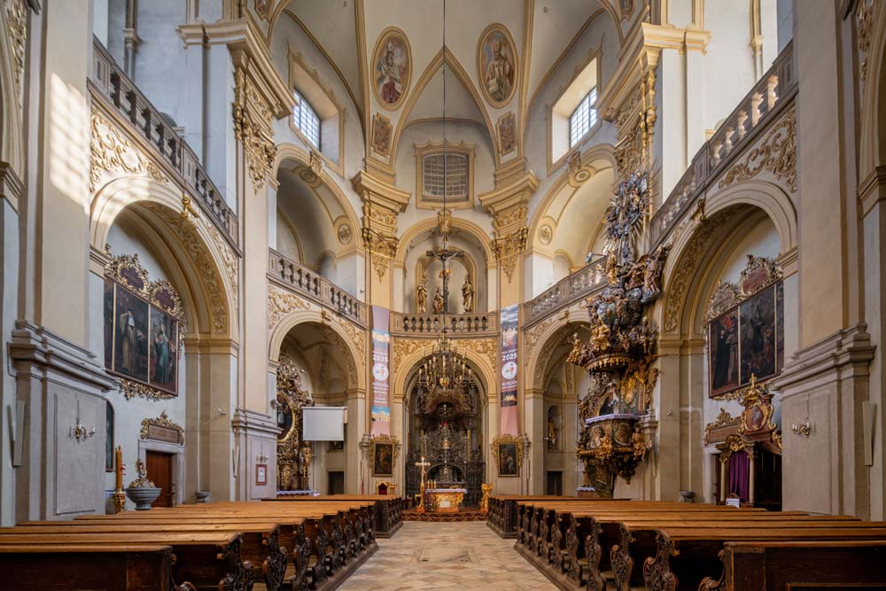 Barokowe sklepienie bazyliki w Wambierzycach widziane od dołu: złocone stiuki, lunety okienne i centralny fresk otoczony medalionami.
