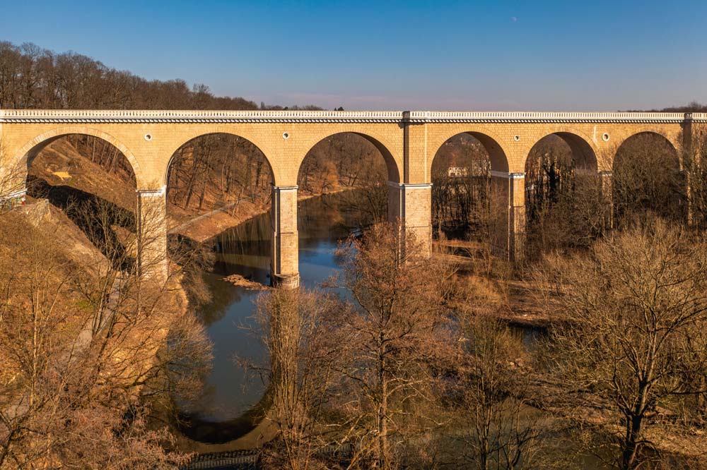 Panoramiczny widok na wieloprzęsłowy, łukowy most kolejowy nad Nysą Łużycką, biegnący wysoko nad doliną i zakolem rzeki.