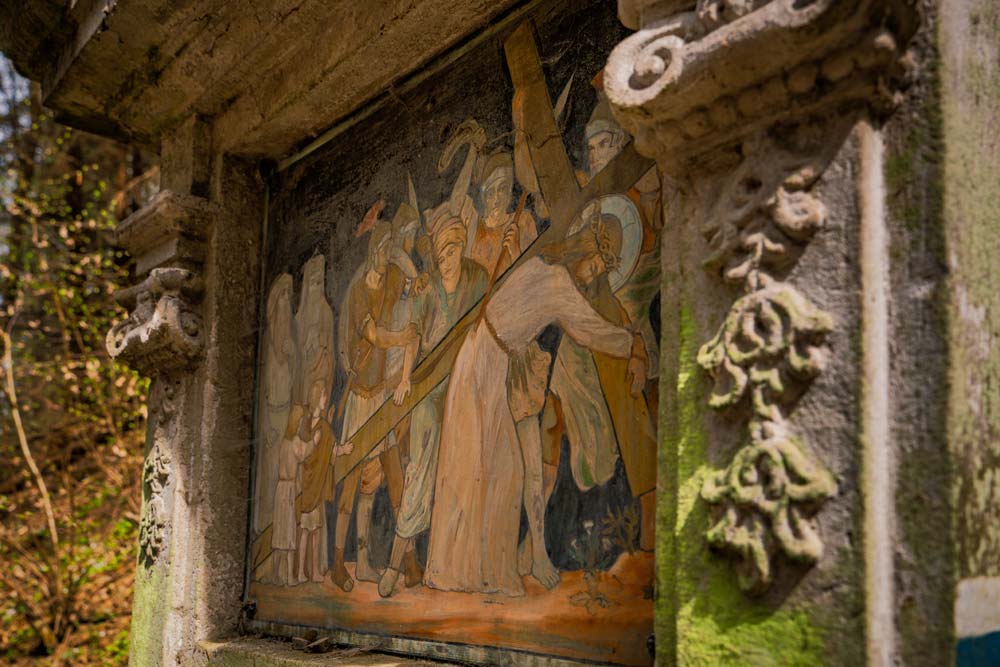 Stacja Drogi Krzyżowej w leśnym wąwozie – kamienna kapliczka z malowidłem w ozdobnej ramie, ujęcie z boku.