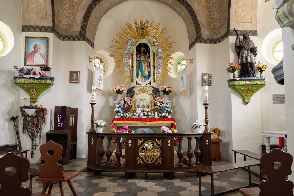 Wnętrze Górskiej Kaplicy Matki Bożej Płaczącej w Bardzie – ołtarz pełen kwiatów, figura Maryi w promienistej glorii.