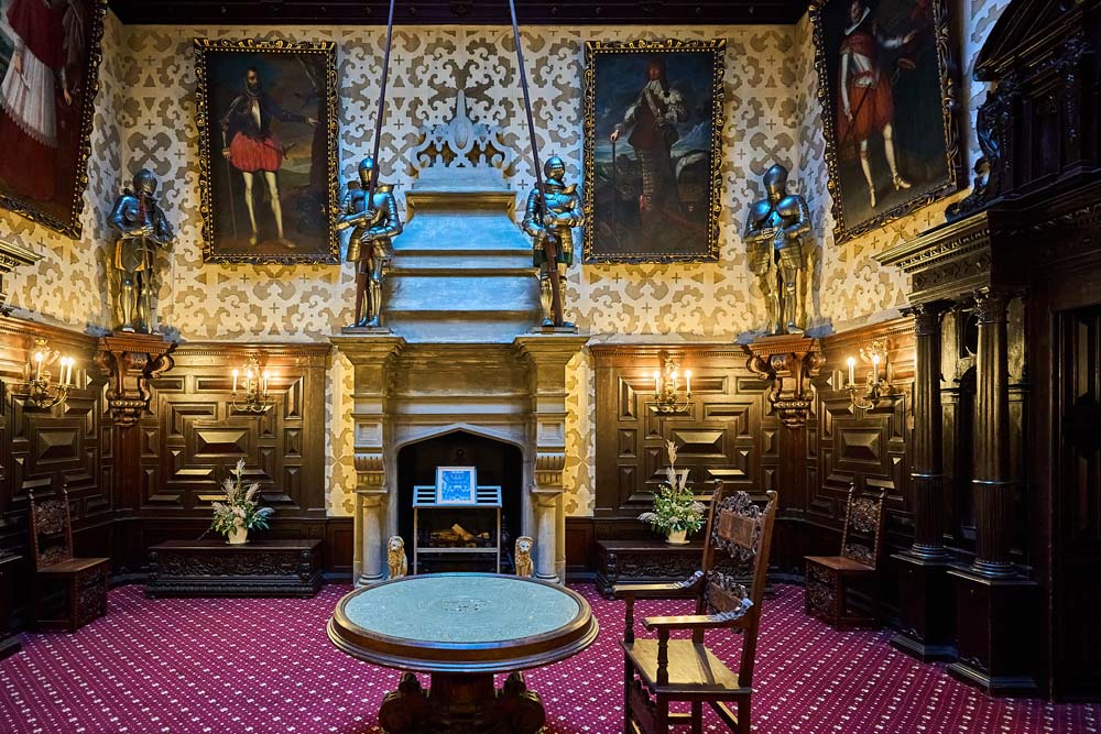 Sala Rycerska w Hradec u Nechanic: kominek, zbroje i portrety na ścianach, a na środku okrągły stół na czerwonym dywanie.