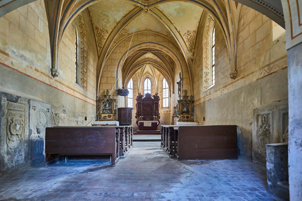 Wnętrze zamkowej kaplicy w Staré Hrady: gotyckie sklepienia, ławki i ołtarz na końcu nawy.