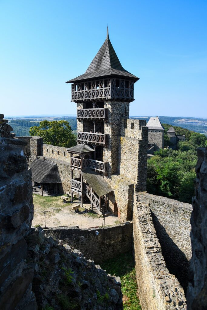 Wieża Helfštýna z drewnianymi galeriami i kamiennymi murami, widziana z przejścia między fragmentami ruin.