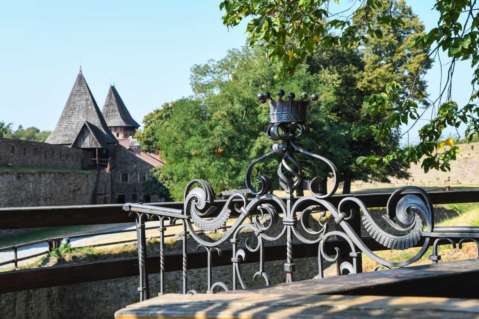 Ozdobna, kuta balustrada z motywem korony na tarasie widokowym zamku; w tle mury i dachy zabudowań.