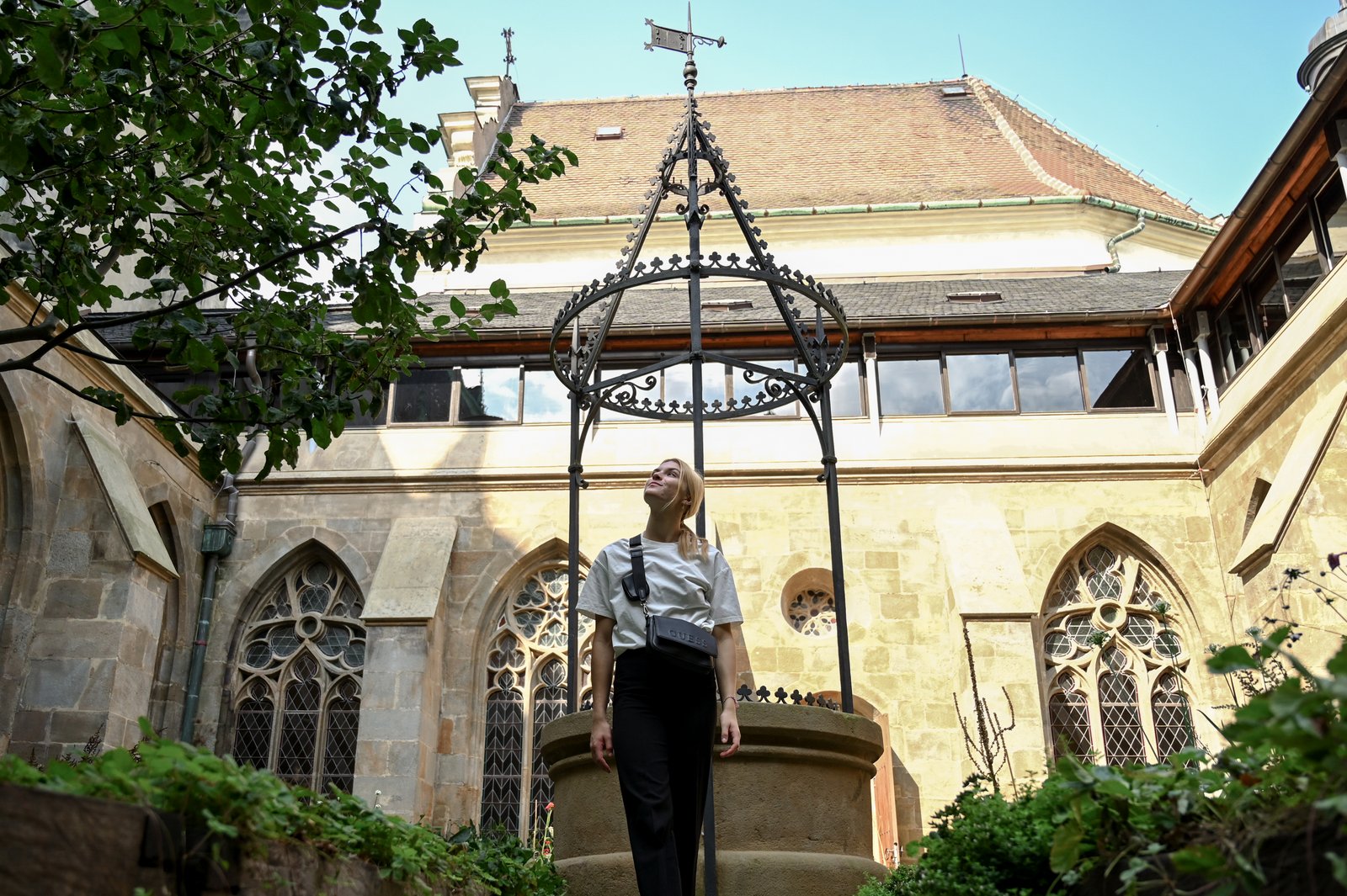 Renesansowa studnia na dziedzińcu rajskim; turystka stoi przy żelaznej konstrukcji, a w tle gotyckie okna i kamienne mury.