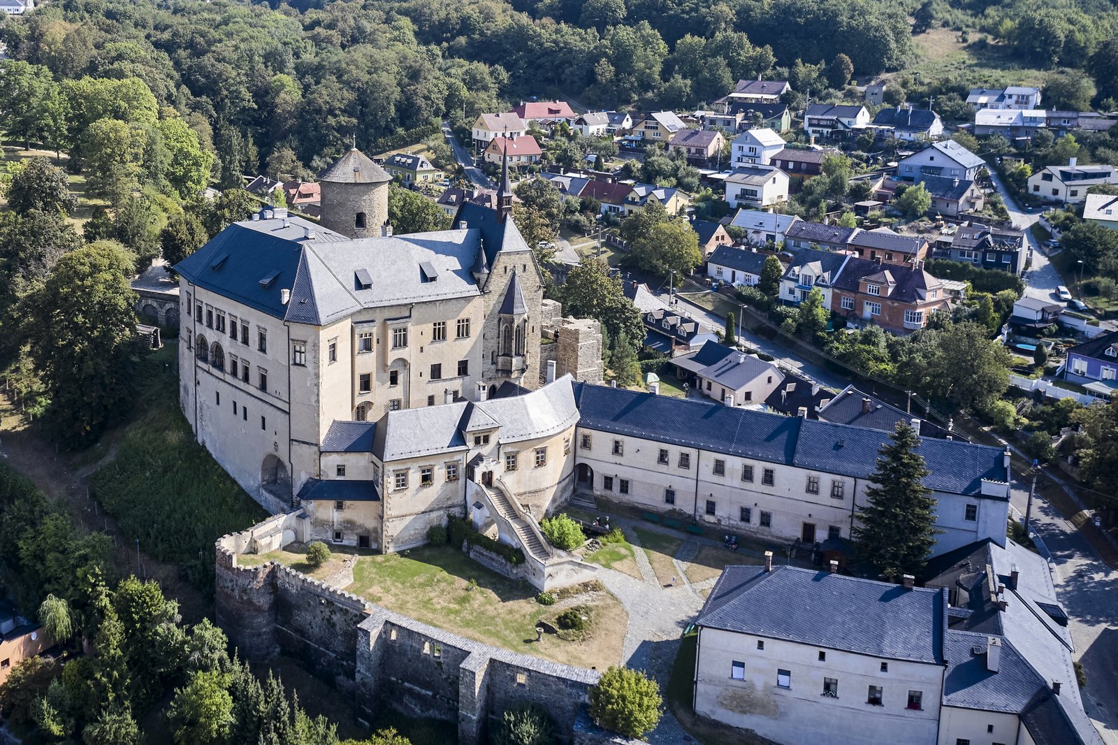 Zamek Šternberk z lotu ptaka: rozległy kompleks z wieżą i niebieskoszarymi dachami, tuż przy zabudowie miasteczka.