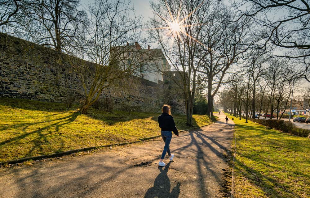 Promenada spacerowa wzdłuż zachowanego odcinka bazaltowych murów obronnych Lubania przy ulicy Podwale, spacerowicz w słońcu