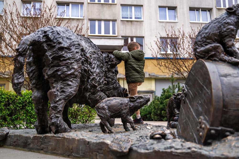 Dziecko w zielonej kurtce dotykające brązowego dzika z pomnika w Świdnicy, obok mały warchlak