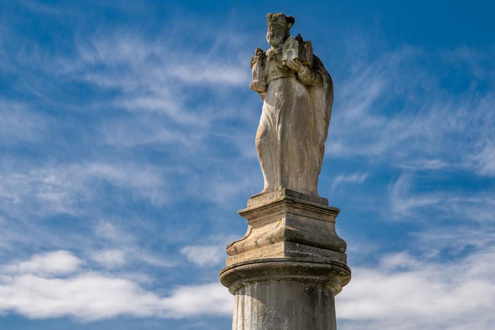 Piaskowcowa figura św. Jadwigi Śląskiej w koronie i książęcym płaszczu z modelem kościoła w dłoni, na tle nieba