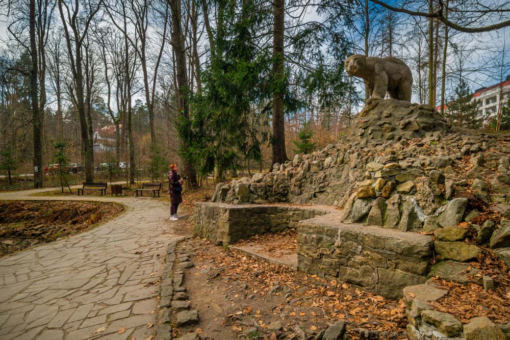 Kopiec z kanciastych bloków miejscowego piaskowca z rzeźbą niedźwiedzia na szczycie, obok turystka dla skali