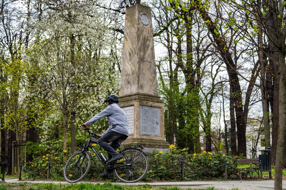 Rowerzysta przejeżdżający alejką parkową obok obelisku w Parku Młodzieżowym w Świdnicy wiosną