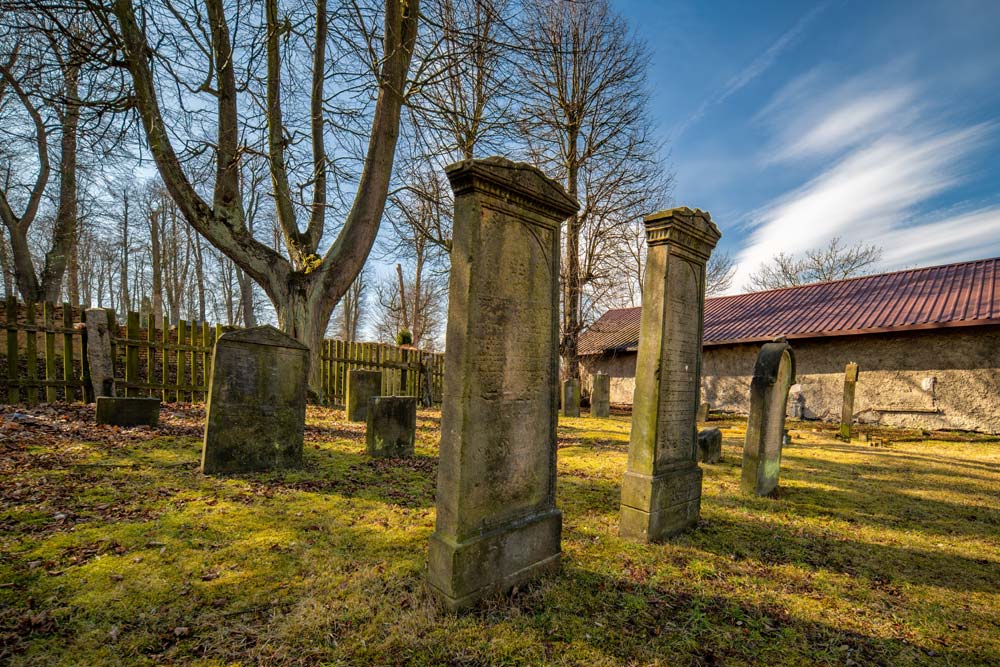 Wysokie stele nagrobne przy kamiennym murze starego cmentarza żydowskiego w Kamiennej Górze
